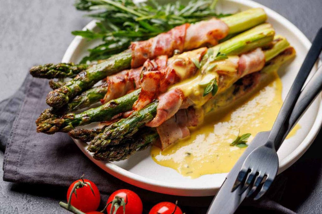 Gericht mit gebratenen grünen Spargelstangen, in Schinken gewickelt auf einem weißen Teller.