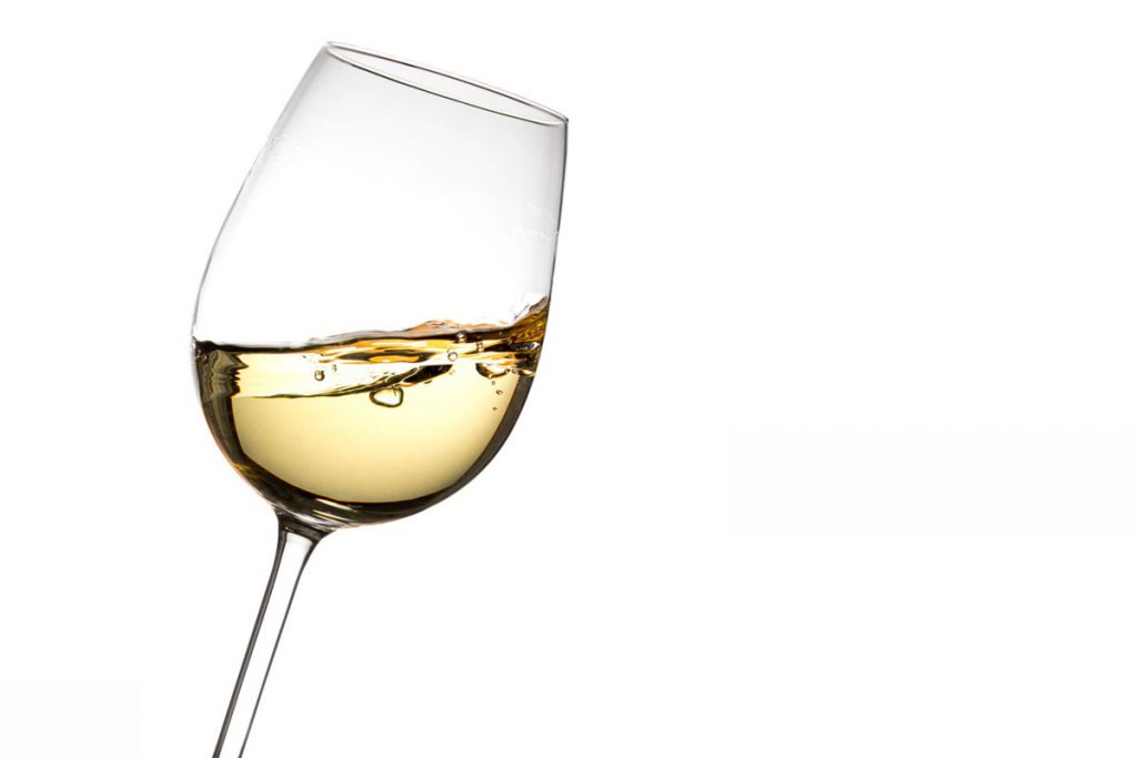 Schräg gehaltenes Weißweinglas mit weißem Wein vor weißem Hintergrund.